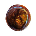 A close-up a small, round, polished brown gemstone with rainbow iridescence