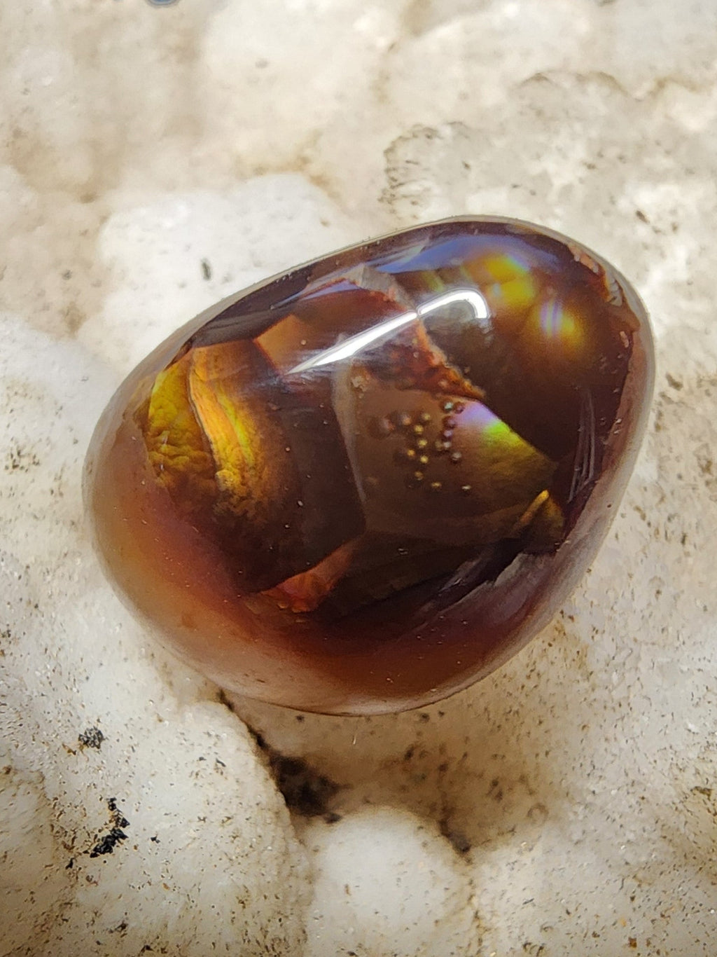 A polished brown gemstone with amber and golden internal inclusions, resting on a textured white crystal cluster.