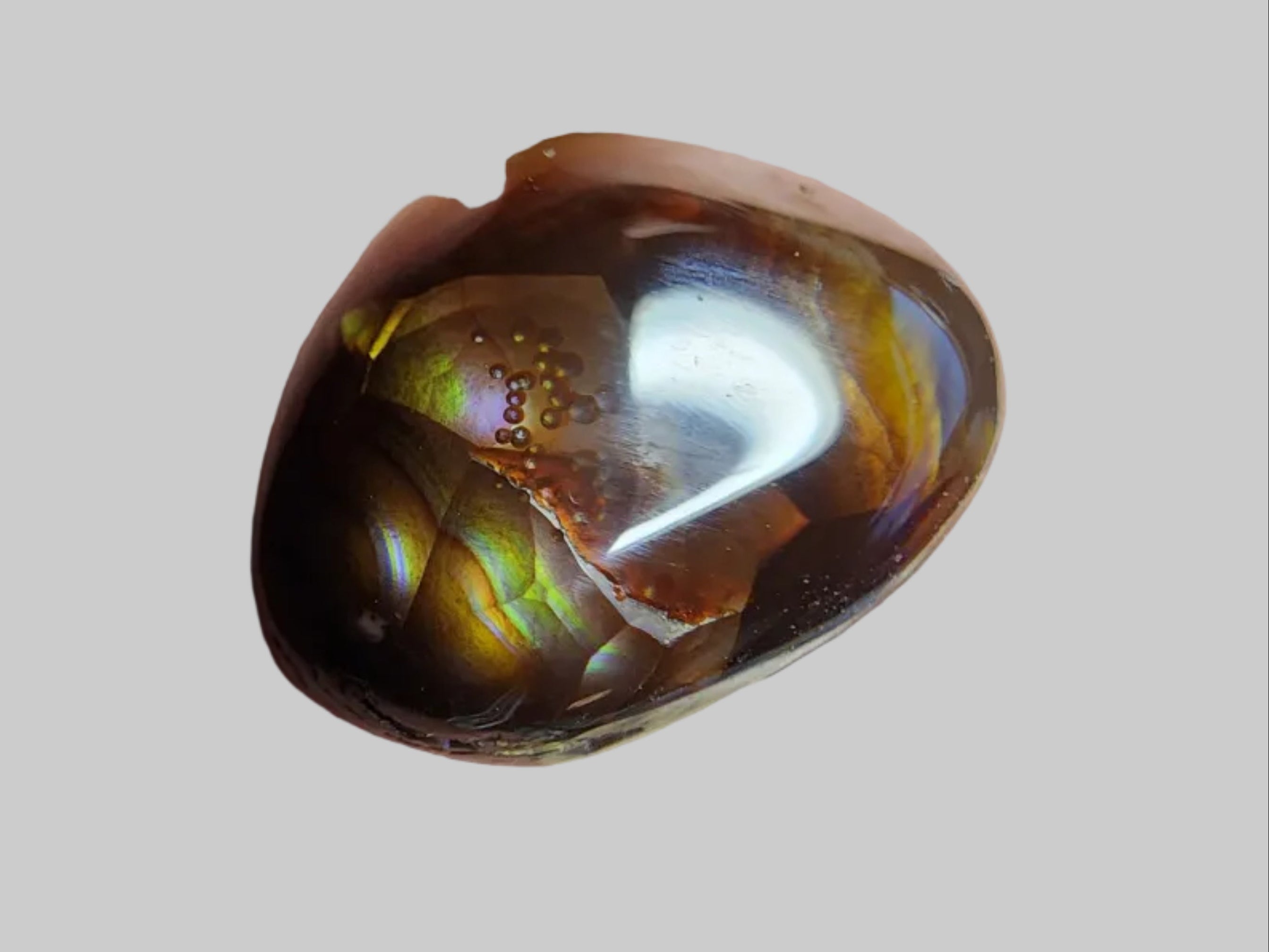 A polished brown gemstone with golden-yellow inclusions, resting on a dark gray textured surface next to a centimeter ruler for scale.
